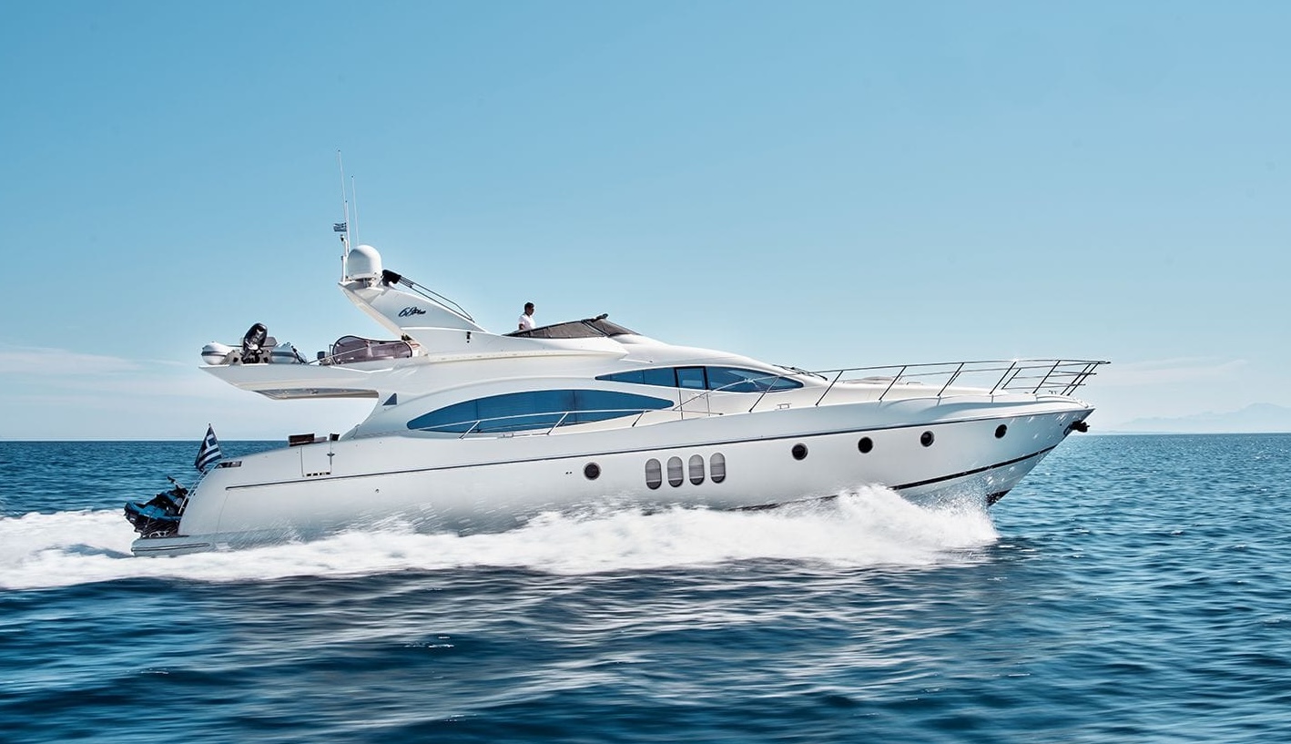 Luxury charter yacht MANU cruising at speed under blue skies, with sleek aerodynamic lines and a Greek flag at the stern.

